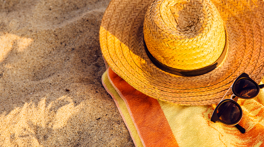 Sunglasses, straw hat and beach towel on sand